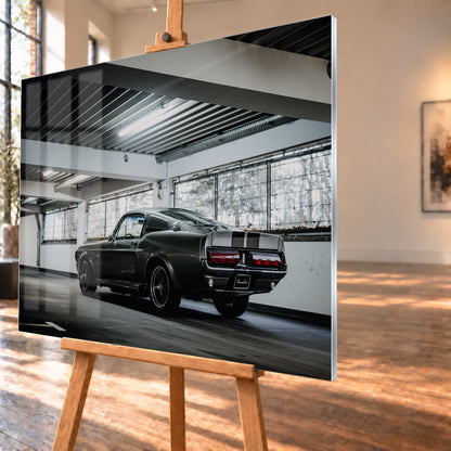 Dunkelgraue Eleanor mit hellen Doppelstreifen in tiefer Heck-Dreiviertelansicht auf einer leeren Parkebene mit weißen Trägern, großen Fenstern und kühlem Deckenlicht; Visualisierung als Acrylglas-Wandbild, schräg von der Seite auf einer Holzstaffelei.