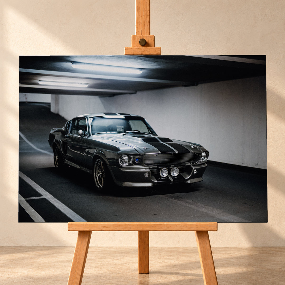 Eleanor mit dunkler Karosserie in frontaler Dreiviertelansicht in einer Beton-Parkgarage; sichtbar sind Längsstreifen, Rundscheinwerfer, zwei zentrale Zusatzleuchten, Fahrbahnmarkierungen und helle Deckenröhren; Visualisierung als Leinwand-Wandbild, frontal auf einer Holzstaffelei.