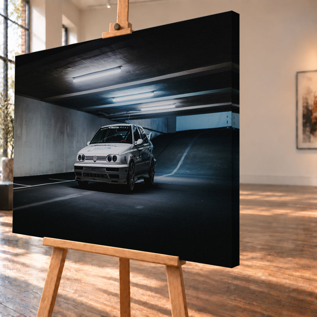 Weißer Volkswagen Jetta in tiefer Dreiviertelansicht von vorn in einer dunklen Beton-Parkgarage. Kühle Deckenleuchten, markierte Stellflächen und eine ansteigende Rampe rahmen das Fahrzeug mit großen Rädern, dunklen Seitengrafiken und Heckflügel; Visualisierung als Leinwand-Wandbild, schräg von der Seite auf einer Holzstaffelei.