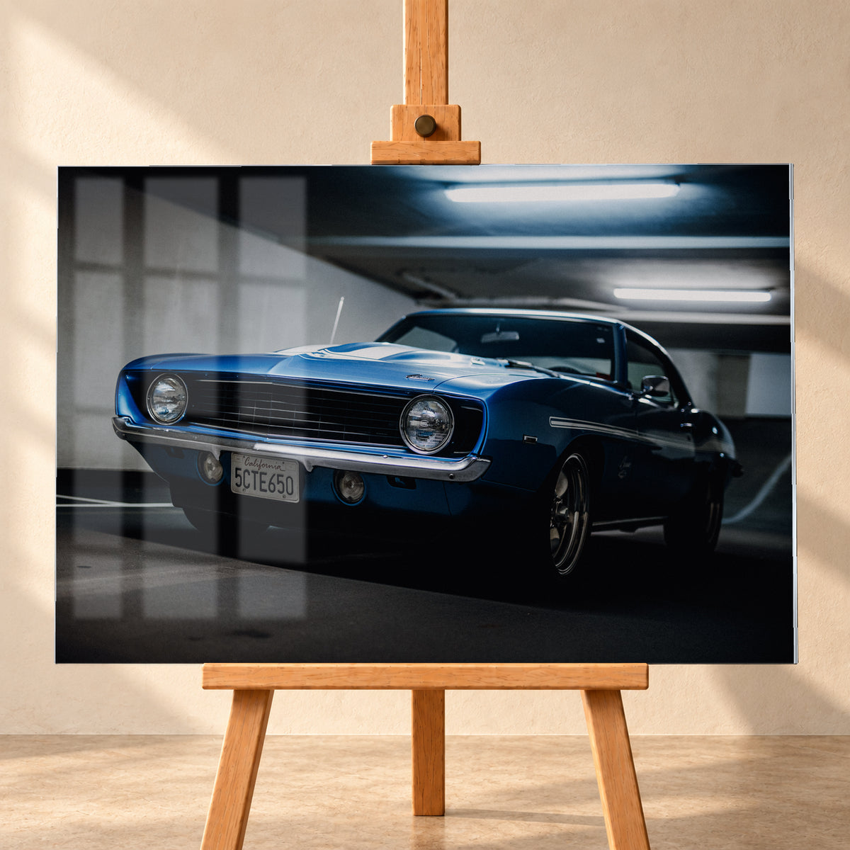 Blauer Yenko Camaro in tiefer Front-Dreiviertelansicht in einer dunklen Parkgarage; sichtbar sind runde Scheinwerfer, schwarzer Kühlergrill, Chromstoßstange, helle Streifen und leuchtende Deckenröhren; Visualisierung als Acrylglas-Wandbild, frontal auf einer Holzstaffelei.
