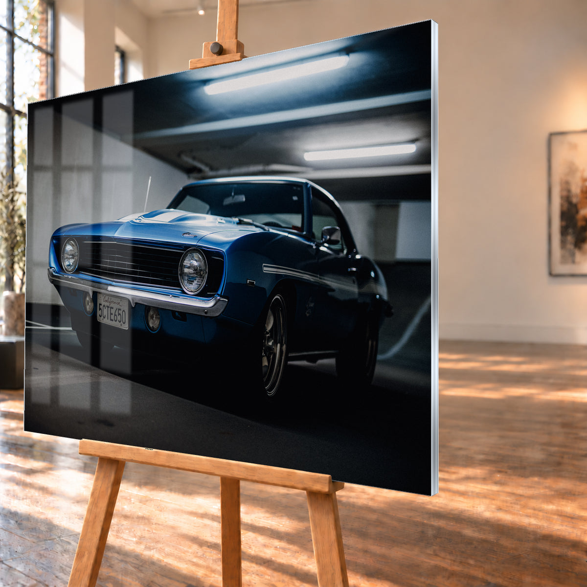 Blauer Yenko Camaro in tiefer Front-Dreiviertelansicht in einer dunklen Parkgarage; sichtbar sind runde Scheinwerfer, schwarzer Kühlergrill, Chromstoßstange, helle Streifen und leuchtende Deckenröhren; Visualisierung als Acrylglas-Wandbild, schräg von der Seite auf einer Holzstaffelei.
