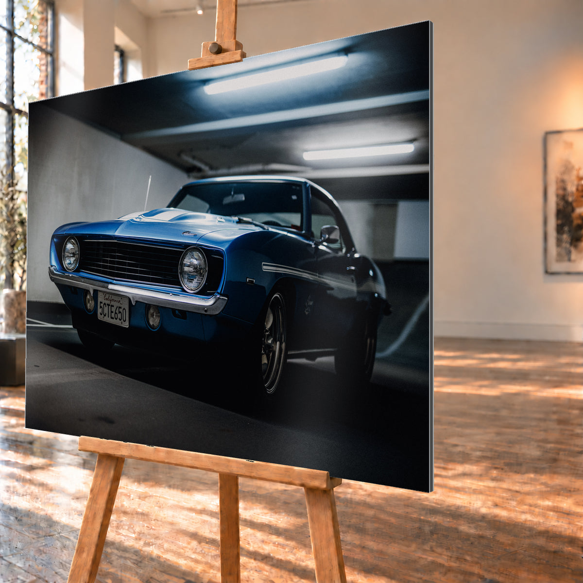 Blauer Yenko Camaro in tiefer Front-Dreiviertelansicht in einer dunklen Parkgarage; sichtbar sind runde Scheinwerfer, schwarzer Kühlergrill, Chromstoßstange, helle Streifen und leuchtende Deckenröhren; Visualisierung als Alu gebürstet-Wandbild, schräg von der Seite auf einer Holzstaffelei.
