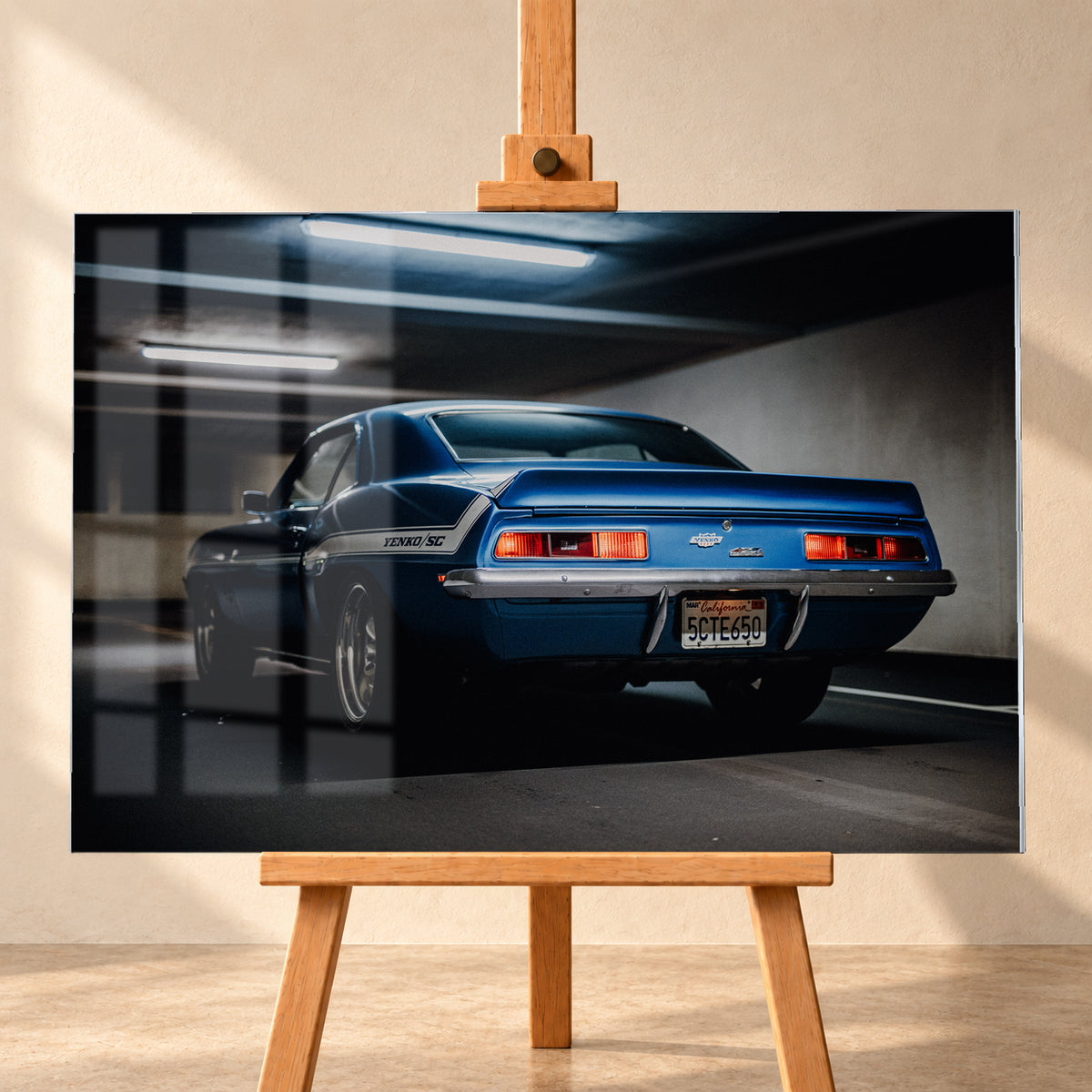 Blauer Chevrolet Camaro Yenko in tiefer Heck-Dreiviertelansicht in einer dunklen Parkgarage; rote Rücklichter, Heckspoiler, YENKO/SC-Seitenstreifen und kühle Deckenleuchten sind sichtbar; Visualisierung als Acrylglas-Wandbild, frontal auf einer Holzstaffelei.