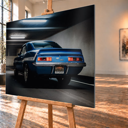 Blauer Chevrolet Camaro Yenko in tiefer Heck-Dreiviertelansicht in einer dunklen Parkgarage; rote Rücklichter, Heckspoiler, YENKO/SC-Seitenstreifen und kühle Deckenleuchten sind sichtbar; Visualisierung als Alu gebürstet-Wandbild, schräg von der Seite auf einer Holzstaffelei.