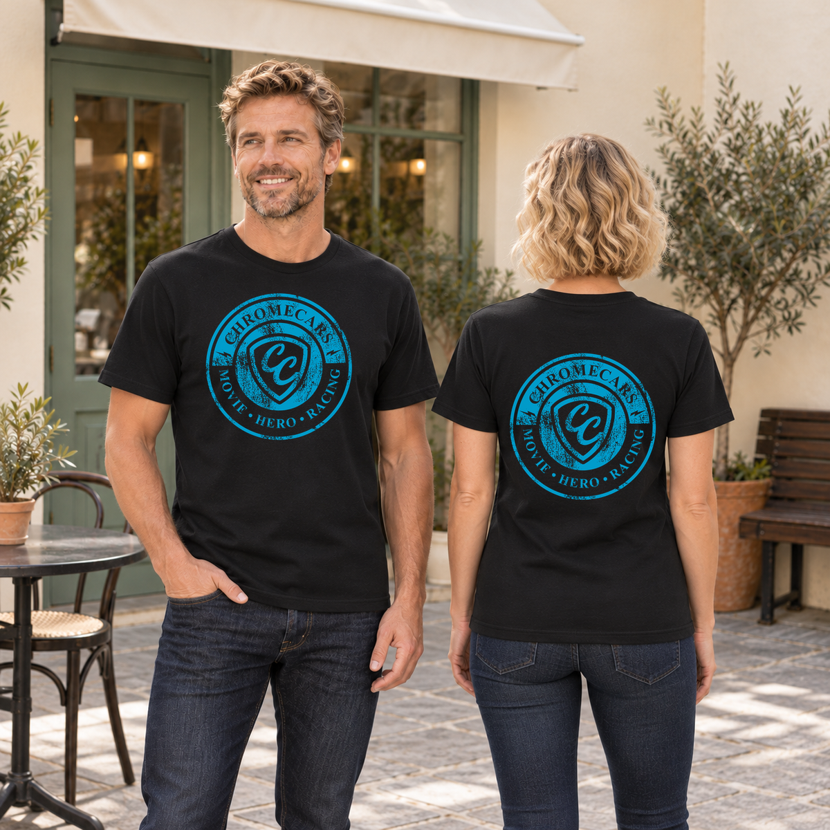 Zwei Personen in schwarzen T-Shirts stehen im Café-Innenhof: der Mann frontal mit einer Hand in der Hosentasche, die Frau rückwärts; blaue Logos vorne beim Mann und hinten bei der Frau.