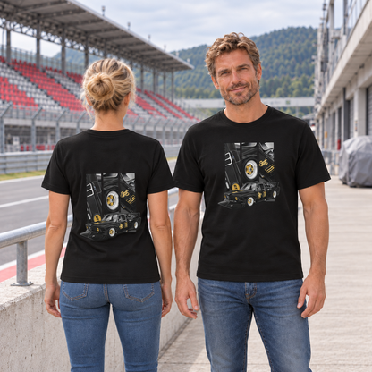 Mann von vorn und Frau von hinten in schwarzen T-Shirts mit BMW-E21-Motiven, an einer Betonbrüstung vor einer rot-grauen Rennstreckentribüne.