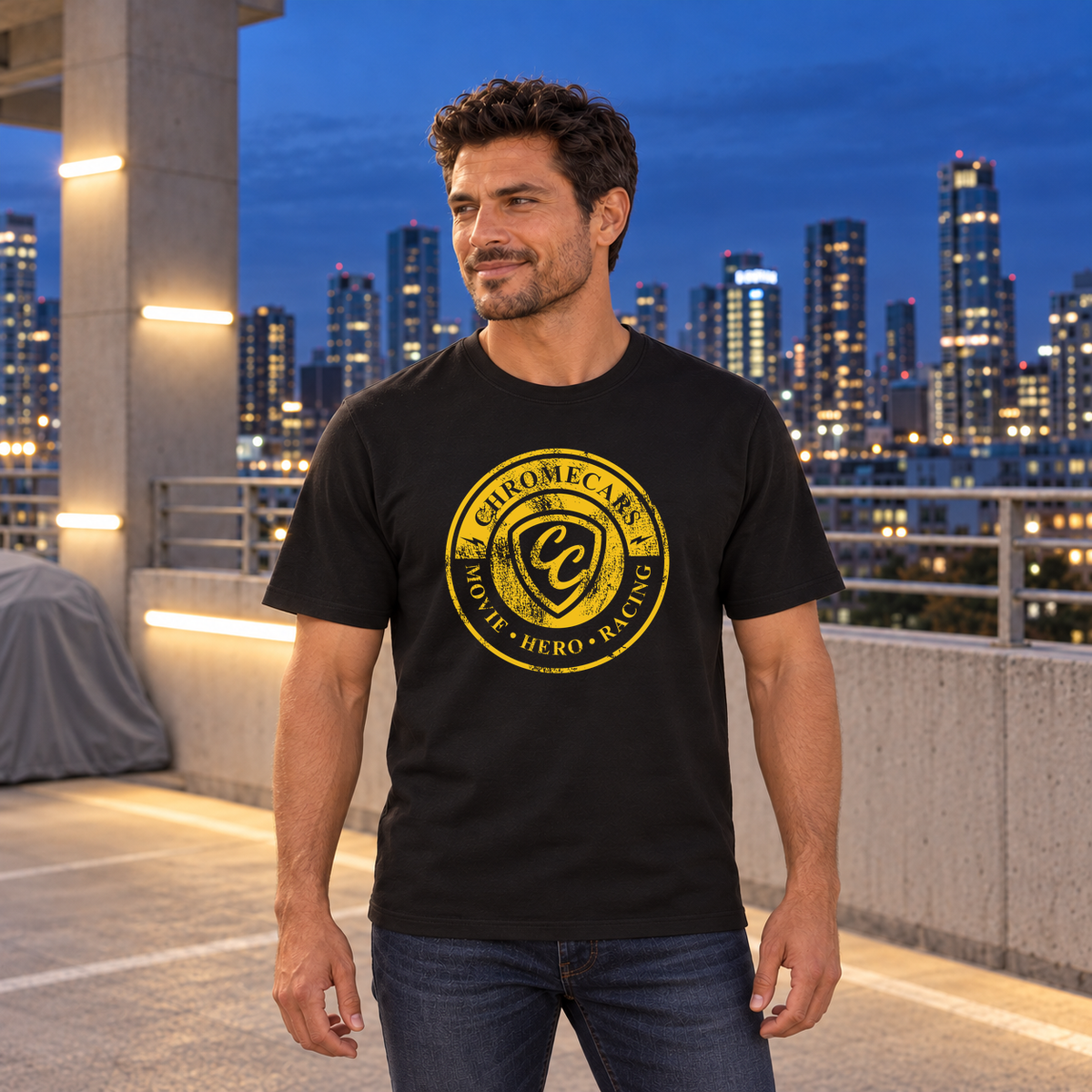 Ein Mann steht mit gesenkten Armen und seitlichem Blick im schwarzen T-Shirt mit gelbem Used Logo vorne auf einem Parkdeck zur blauen Stunde.