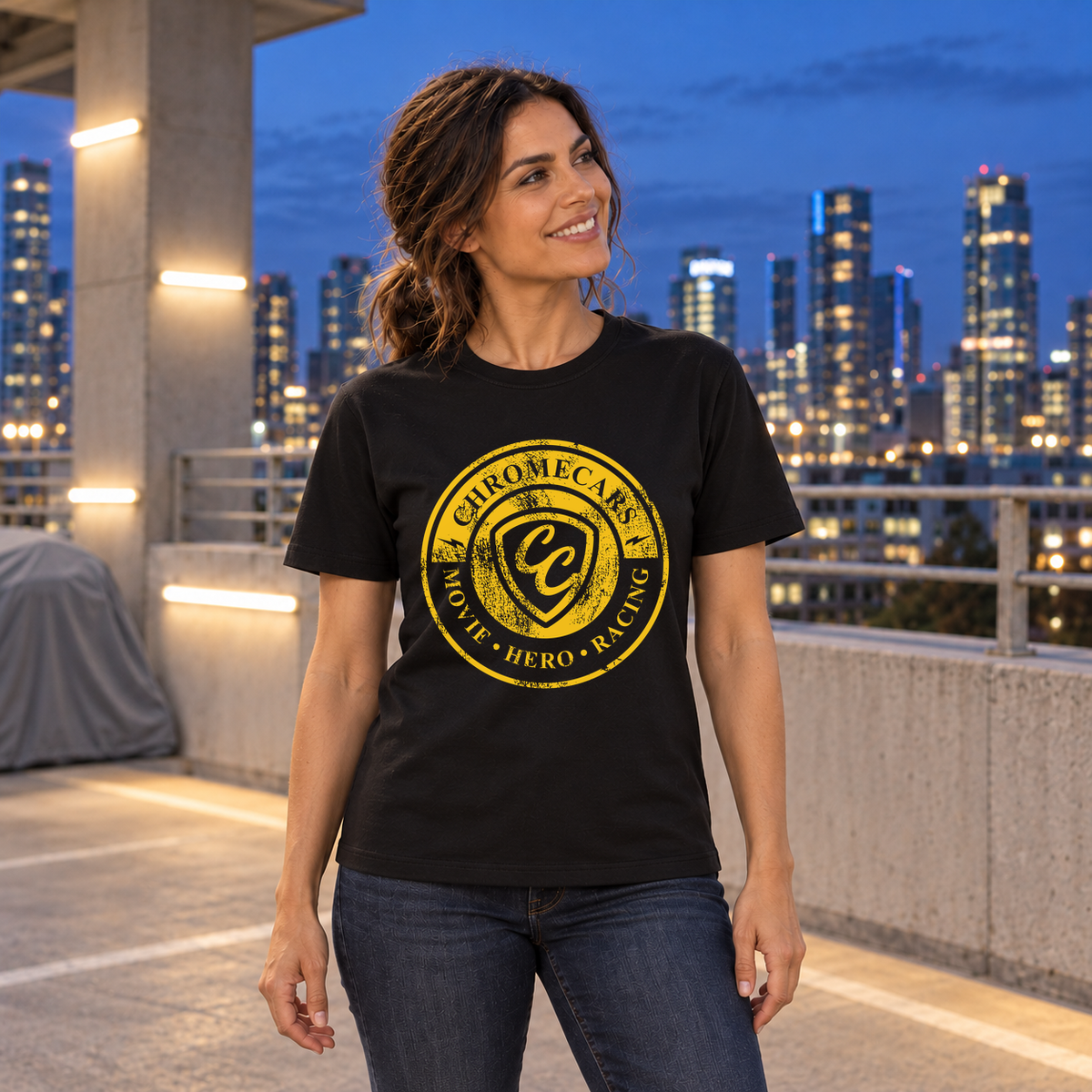 Eine Frau steht lächelnd mit seitlich angehobenem Blick im schwarzen T-Shirt mit gelbem Used Logo vorne auf einem Parkdeck zur blauen Stunde.