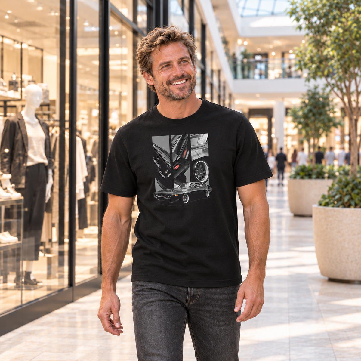 Mann von vorn im schwarzen T-Shirt mit GTX-Motiv auf der Vorderseite, in einer Einkaufspassage mit Schaufenstern.