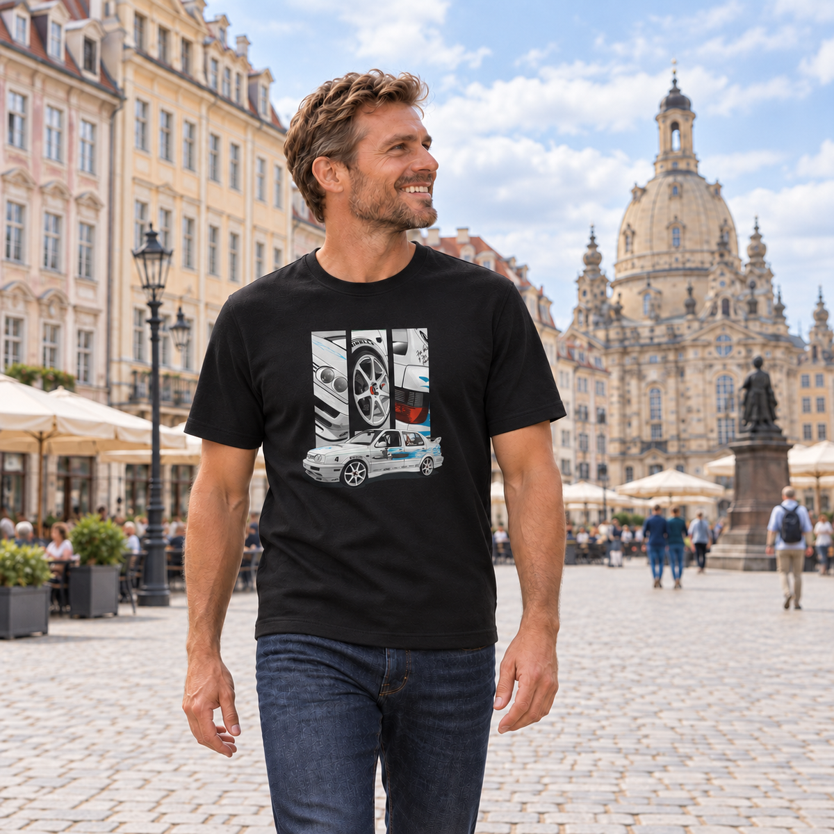Mann von vorn im schwarzen T-Shirt mit Jetta-Motiv auf der Vorderseite, auf einem gepflasterten Stadtplatz vor historischen Gebäuden und einer Kuppelkirche.
