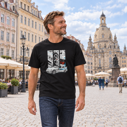 Mann von vorn im schwarzen T-Shirt mit Jetta-Motiv auf der Vorderseite, auf einem gepflasterten Stadtplatz vor historischen Gebäuden und einer Kuppelkirche.