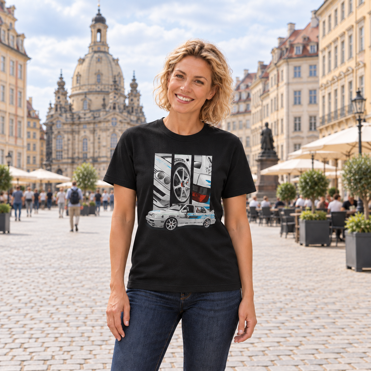 Frau von vorn im schwarzen T-Shirt mit Jetta-Motiv auf der Vorderseite, auf einem gepflasterten Stadtplatz vor historischen Gebäuden und einer Kuppelkirche.