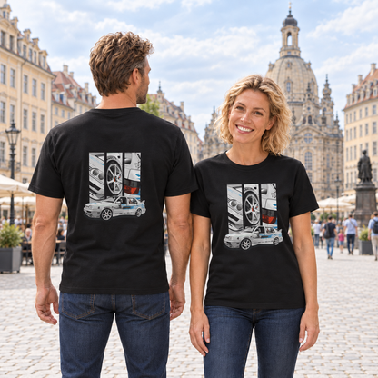 Frau von vorn und Mann von hinten in schwarzen T-Shirts mit Jetta-Motiven, auf einem gepflasterten Stadtplatz vor historischen Gebäuden und einer Kuppelkirche.