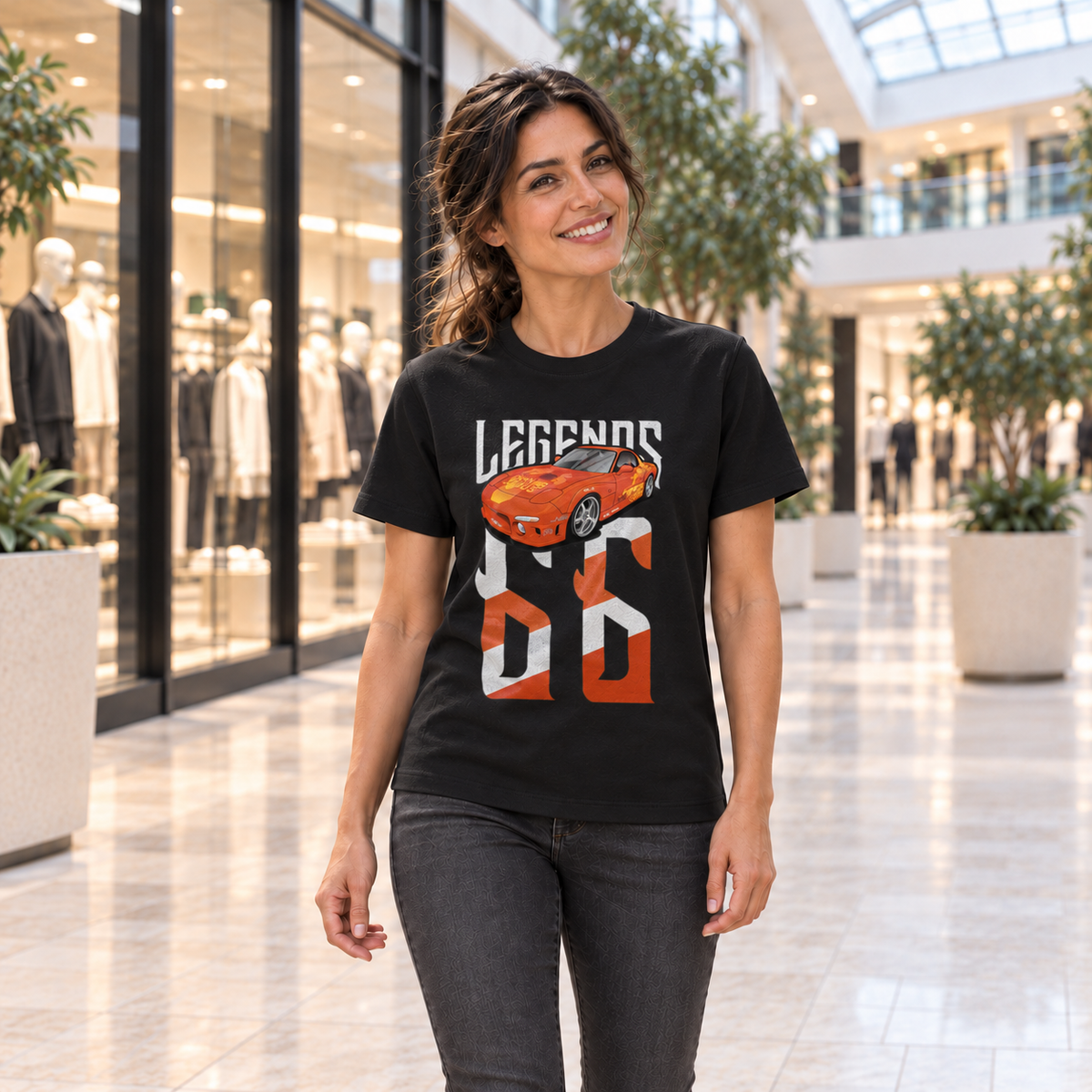 Frau von vorn im schwarzen T-Shirt mit Orange-Julius-Legends-Motiv auf der Vorderseite, im Atrium eines Einkaufszentrums mit Glasdach.