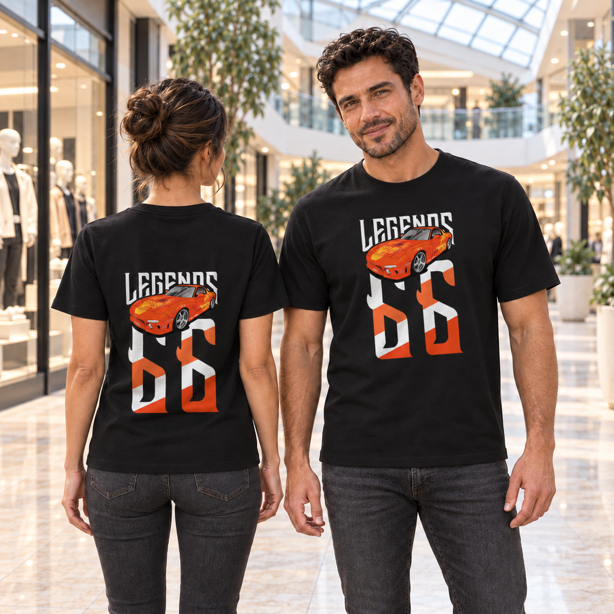 Mann von vorn und Frau von hinten in schwarzen T-Shirts mit Orange-Julius-Legends-Motiven, im Atrium eines Einkaufszentrums mit Glasdach.