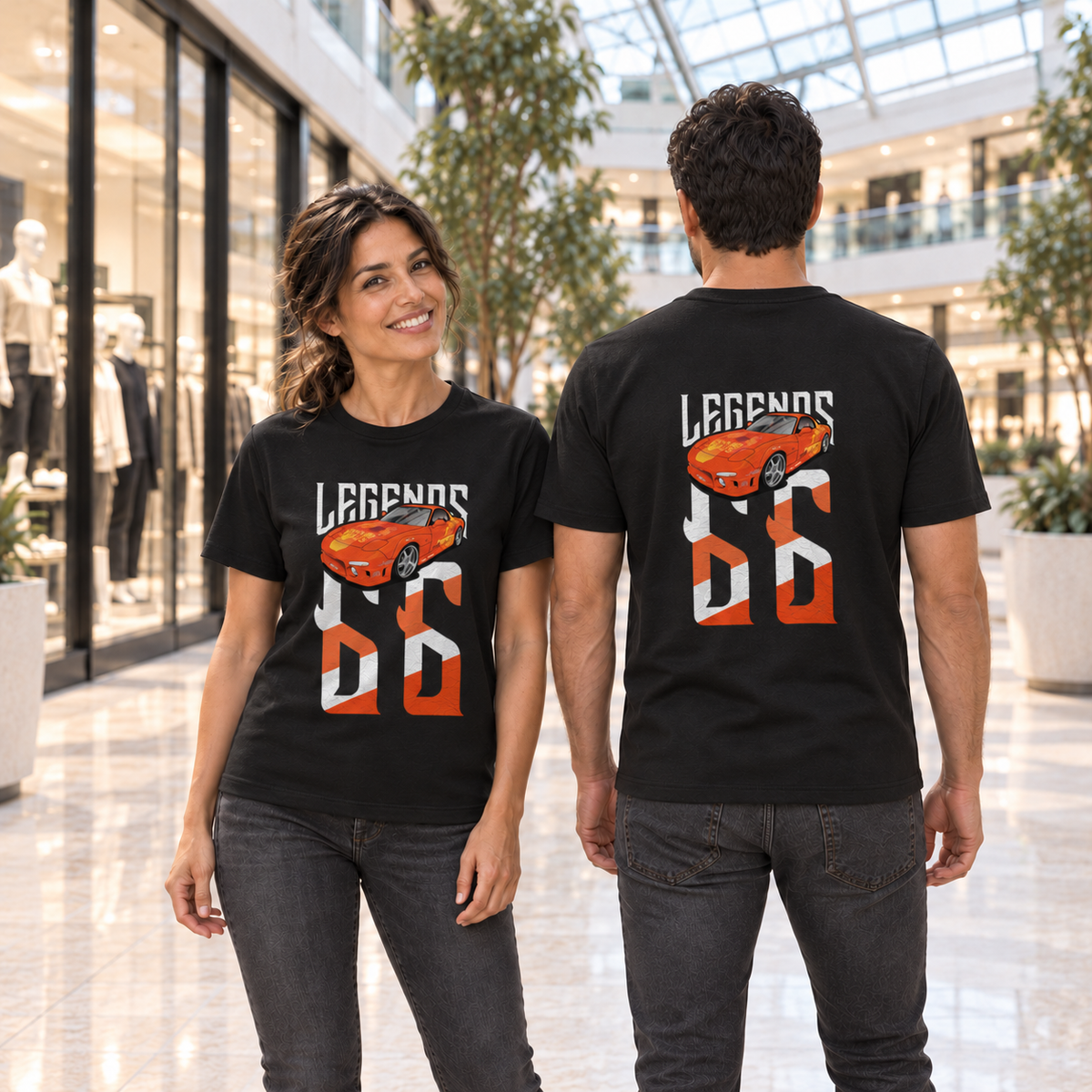 Frau von vorn und Mann von hinten in schwarzen T-Shirts mit Orange-Julius-Legends-Motiven, im Atrium eines Einkaufszentrums mit Glasdach.
