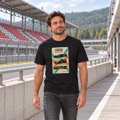 Mann von vorn im schwarzen T-Shirt mit Racing-Legends-Motiv auf der Vorderseite, an einer Betonbrüstung vor einer rot-grauen Rennstreckentribüne.