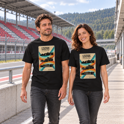 Mann und Frau in schwarzen T-Shirts mit Racing-Legends-Motiven vorn, an einer Betonbrüstung vor einer rot-grauen Rennstreckentribüne.
