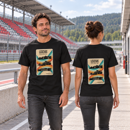 Mann von vorn und Frau von hinten in schwarzen T-Shirts mit Racing-Legends-Motiven, an einer Betonbrüstung vor einer rot-grauen Rennstreckentribüne.
