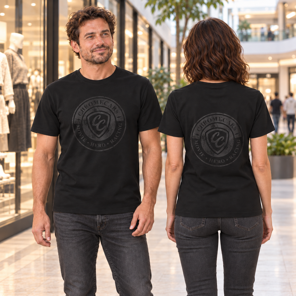 Zwei Personen stehen im Shopping-Center, der Mann von vorn und die Frau von hinten; schwarze T-Shirts mit sehr dezenten schwarzen Used-Logos auf Brust beziehungsweise Rücken.