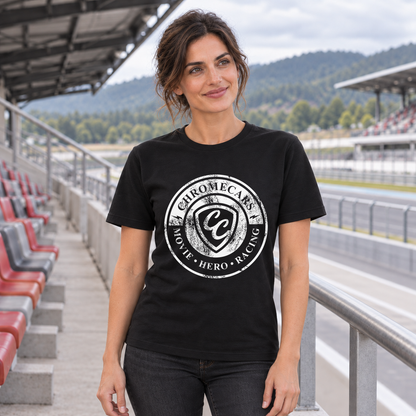 Eine Frau im schwarzen T-Shirt mit weißem Used Logo vorne steht mit gesenkten Armen und blickt seitlich. Sie befindet sich im Tribünengang der Rennstrecke neben rot-grauen Sitzen und einem Geländer.