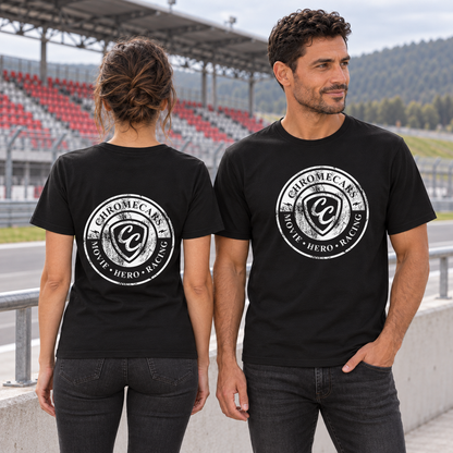 Zwei Personen in schwarzen T-Shirts: links eine Frau mit weißem Used Logo hinten, rechts ein Mann mit weißem Logo vorne und einer Hand in der Hosentasche. Sie stehen an der Rennstrecke vor der rot-grauen Tribüne.