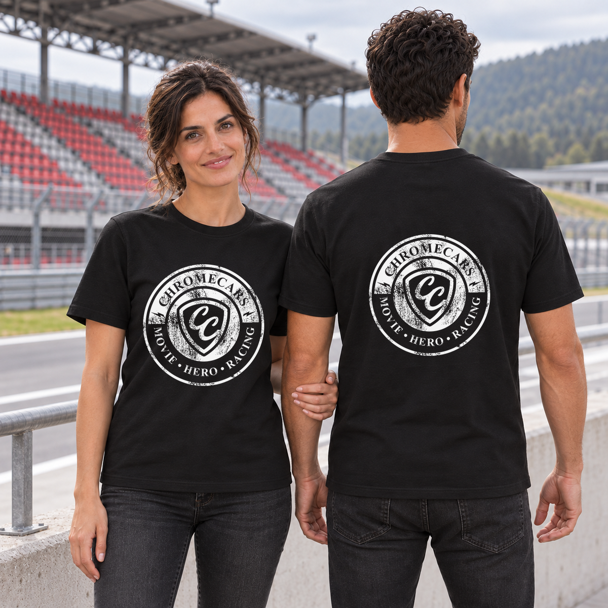 Zwei Personen in schwarzen T-Shirts: Eine Frau mit weißem Used Logo vorne hält den Arm eines rückwärts zur Kamera stehenden Mannes mit weißem Logo hinten. Im Hintergrund liegen Rennstrecke und rot-graue Tribüne.