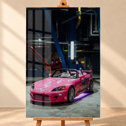 Frontale Produktvisualisierung eines Acrylglasbilds im Hochformat auf einer Holzstaffelei vor heller Wand. Fensterreflexionen überlagern das Motiv des pinken Honda S2000 aus „2 Fast 2 Furious“, der schräg von vorn in einer dunklen Industriehalle zu sehen ist.