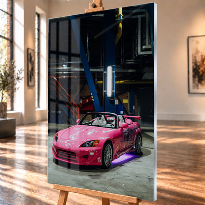 Das hochformatige Acrylglasbild ist schräg auf einer Staffelei visualisiert, mit sichtbarer rechter Kante und Fensterreflexionen auf der Bildfläche. Es zeigt den pinken Honda S2000 aus „2 Fast 2 Furious“ mit weißem Dekor und violetter Unterbodenbeleuchtung in einer Industriehalle.