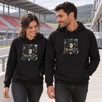 Paar in schwarzen Hoodies geht nebeneinander durch die Rennstreckentribüne. Beide Vorderseiten zeigen den schwarzen Rennwagen mit goldfarbenen Akzenten und drei hochformatigen Feldern.