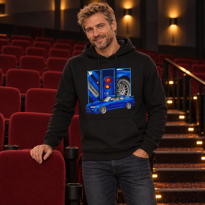 Mann im schwarzen Hoodie mit blauem Coupé und drei Detailfeldern auf der Vorderseite, stehend zwischen roten Kinositzen mit einer Hand an einer Lehne.