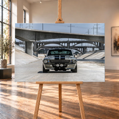 Raumansicht als Visualisierung: Ein querformatiges Wandbild aus gebürstetem Aluminium steht auf einer Holzstaffelei zwischen hohen Fenstern und sonnenbeschienenem Holzboden. Es zeigt den Ford Mustang Shelby GT500 „Eleanor“ frontal vor Betonbrücken.