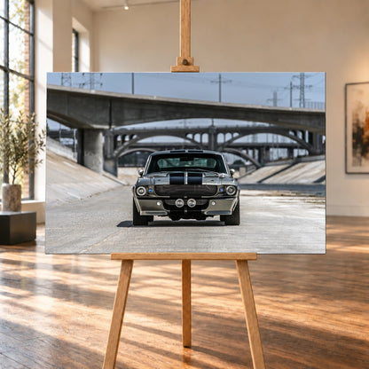 Raumvisualisierung mit einer querformatigen Leinwand auf einer Holzstaffelei, umgeben von hohen Fenstern und sonnenbeschienenem Holzboden. Das Bild zeigt den Ford Mustang Shelby GT500 „Eleanor“ in Frontalansicht im Betonkanal unter Bogenbrücken.