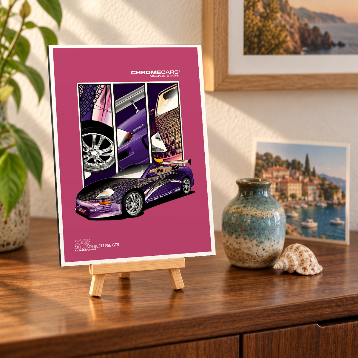 Mockup einer kleinen hochformatigen Alu-Dibond-Bildplatte auf einer Holzstaffelei, leicht schräg von vorn auf einer Holzkommode gezeigt. Motiv: violettes Mitsubishi-Eclipse-Cabrio mit gemusterter Karosserie, Heckflügel und drei Fahrzeugdetails auf pinkem Grund. Pflanze, Vase, Muschel und Küstenbilder sind Szenerie, nicht Lieferumfang.