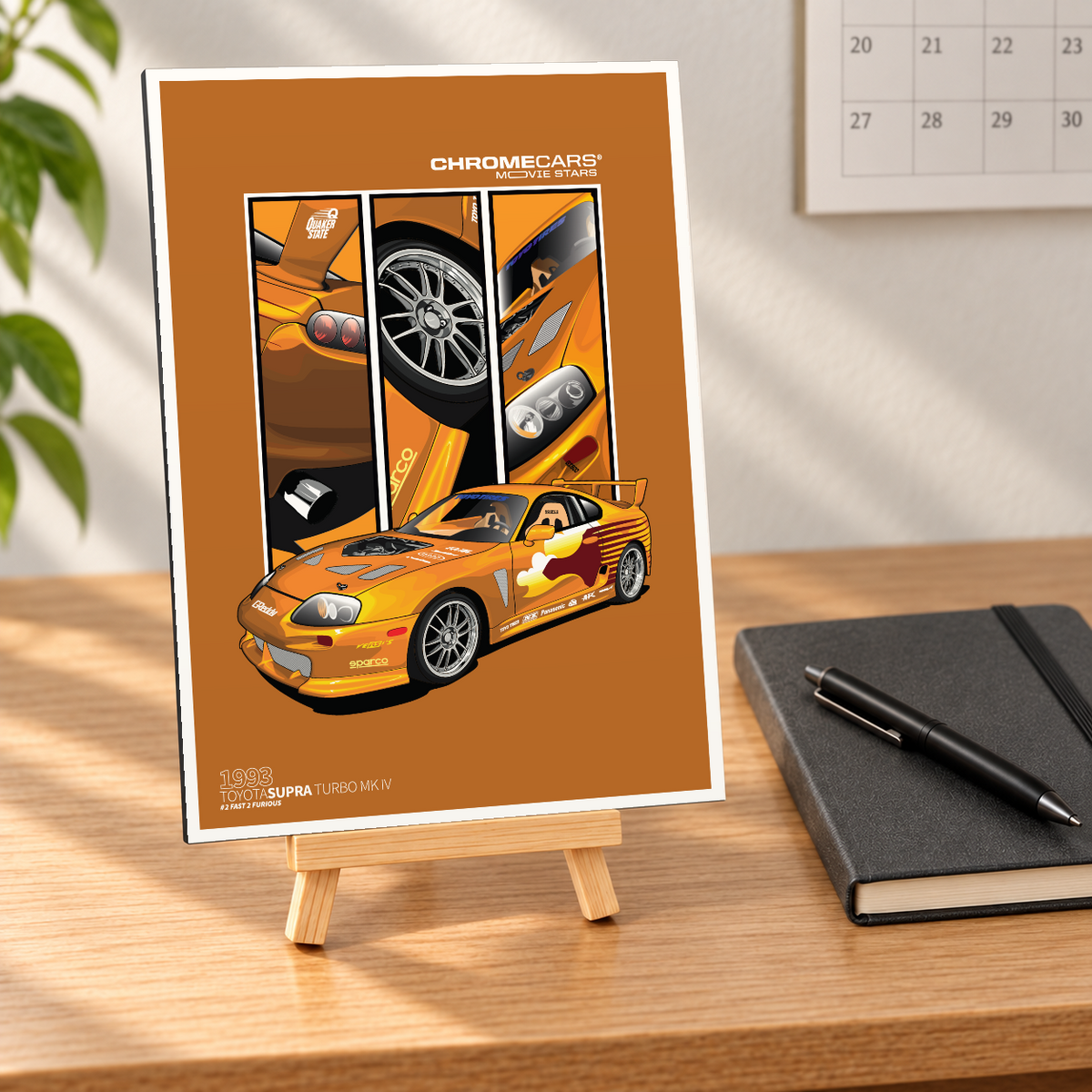 Mockup einer kleinen hochformatigen Alu-Dibond-Bildplatte auf einer Holzstaffelei, nahezu frontal auf einem hellen Holzschreibtisch gezeigt. Das Motiv zeigt den orangefarbenen Fast 2 „Slap Jack“ Supra in vorderer Dreiviertelansicht vor drei senkrechten Detailbildern von Heck, Rad und Front auf braunorangefarbenem Grund. Schwarzes Notizbuch mit Stift, Wandkalender und Pflanze bilden die Szenerie.