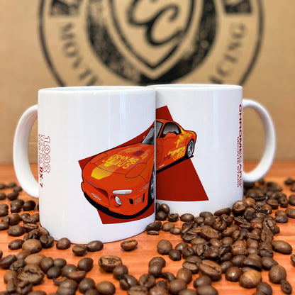 Zwei weiße Tassen mit orangefarbenem Mazda-RX-7-Motiv zwischen Kaffeebohnen.