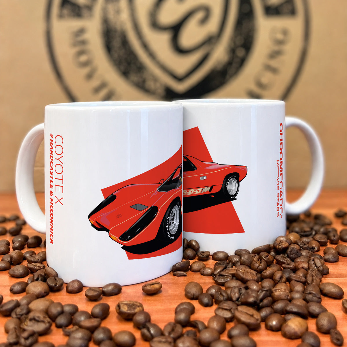 Zwei weiße Tassen mit rotem Coyote-X-Druck zwischen Kaffeebohnen.