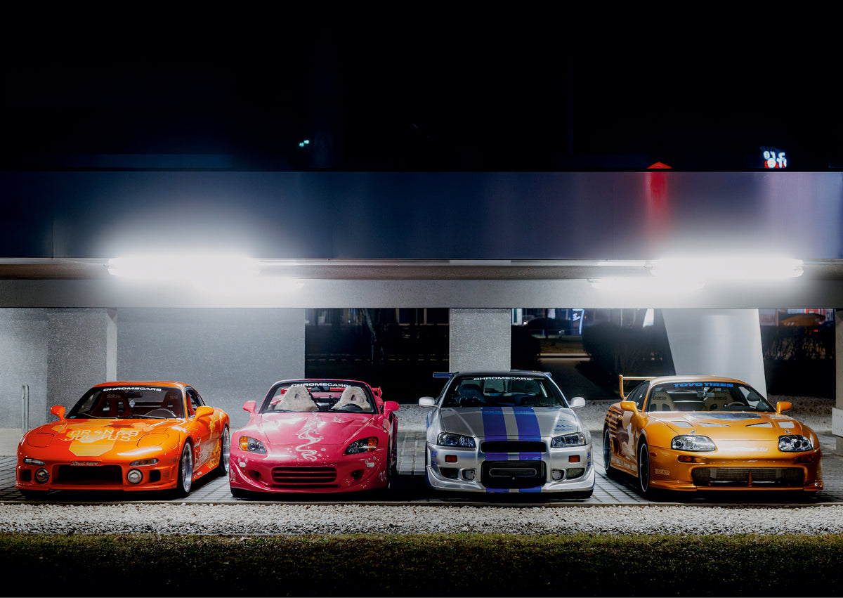 Vier Autos nebeneinander von vorn unter hellen Leuchten: links ein orangefarbener Mazda RX-7, daneben ein pinker, offener Honda S2000 mit weißen Sitzbezügen, ein silberner Nissan Skyline GT-R R34 mit blauen Streifen und rechts eine goldfarbene Toyota Supra mit Heckflügel. Graue Pfeiler, Pflaster und heller Kies vor dunklem Hintergrund.