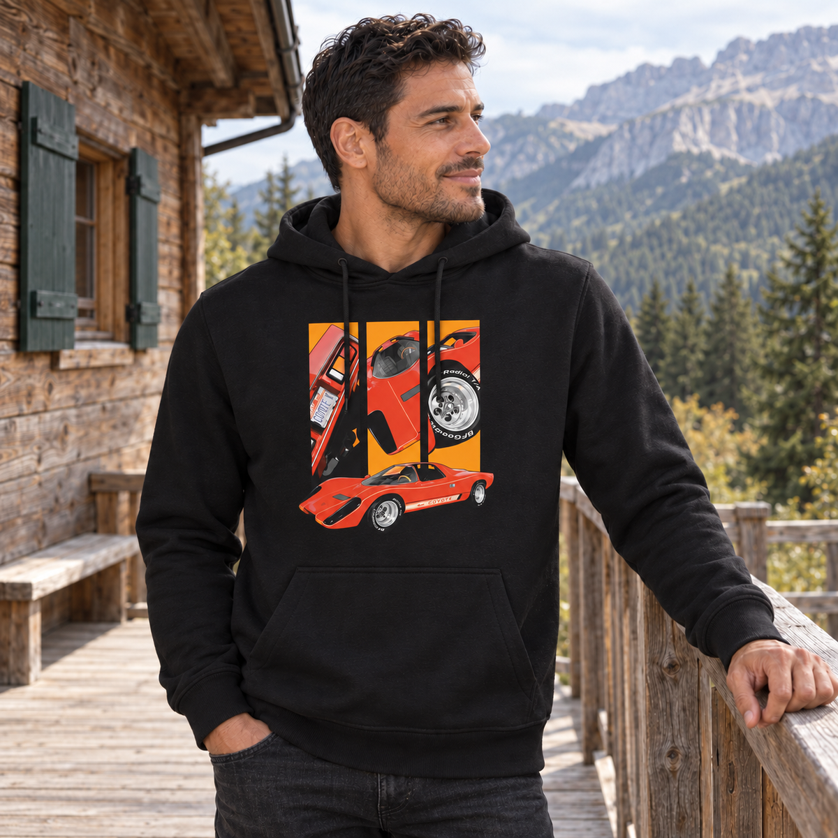 Mann im schwarzen Hoodie steht am Holzgeländer einer Berghüttenterrasse und blickt in die Ferne. Vorn ist ein rotes Fahrzeug unter drei orangefarbenen Detailfeldern sichtbar.