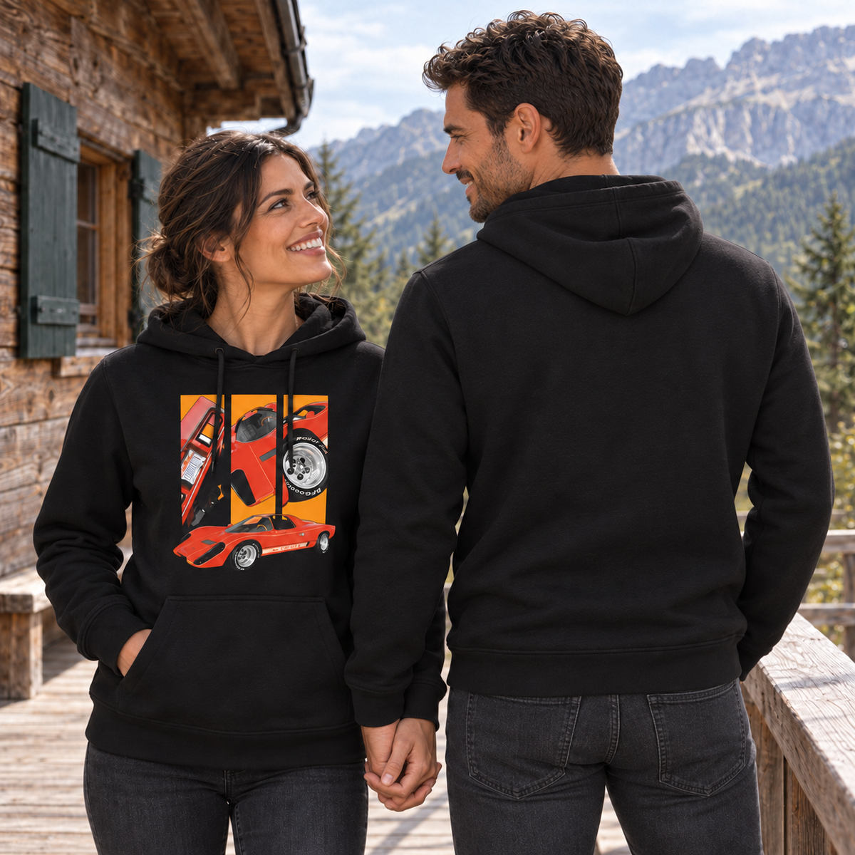 Paar in schwarzen Hoodies steht auf einer Holzterrasse mit Bergblick. Die Frau zeigt das rote Frontmotiv, der Mann seinen unbedruckten Rücken.