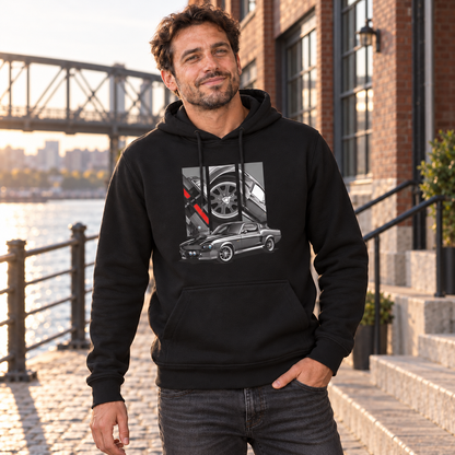 Mann im schwarzen Eleanor-Hoodie am Ufer vor einer Backsteinfassade; graues Fahrzeugmotiv und drei Detailfelder auf der Vorderseite.