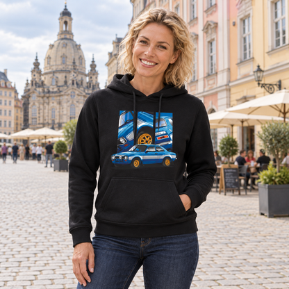 Frau im schwarzen Hoodie steht lächelnd auf einem gepflasterten Altstadtplatz. Ihre Vorderseite zeigt das blaue Fahrzeugmotiv mit hellem Seitenstreifen und drei Feldern.