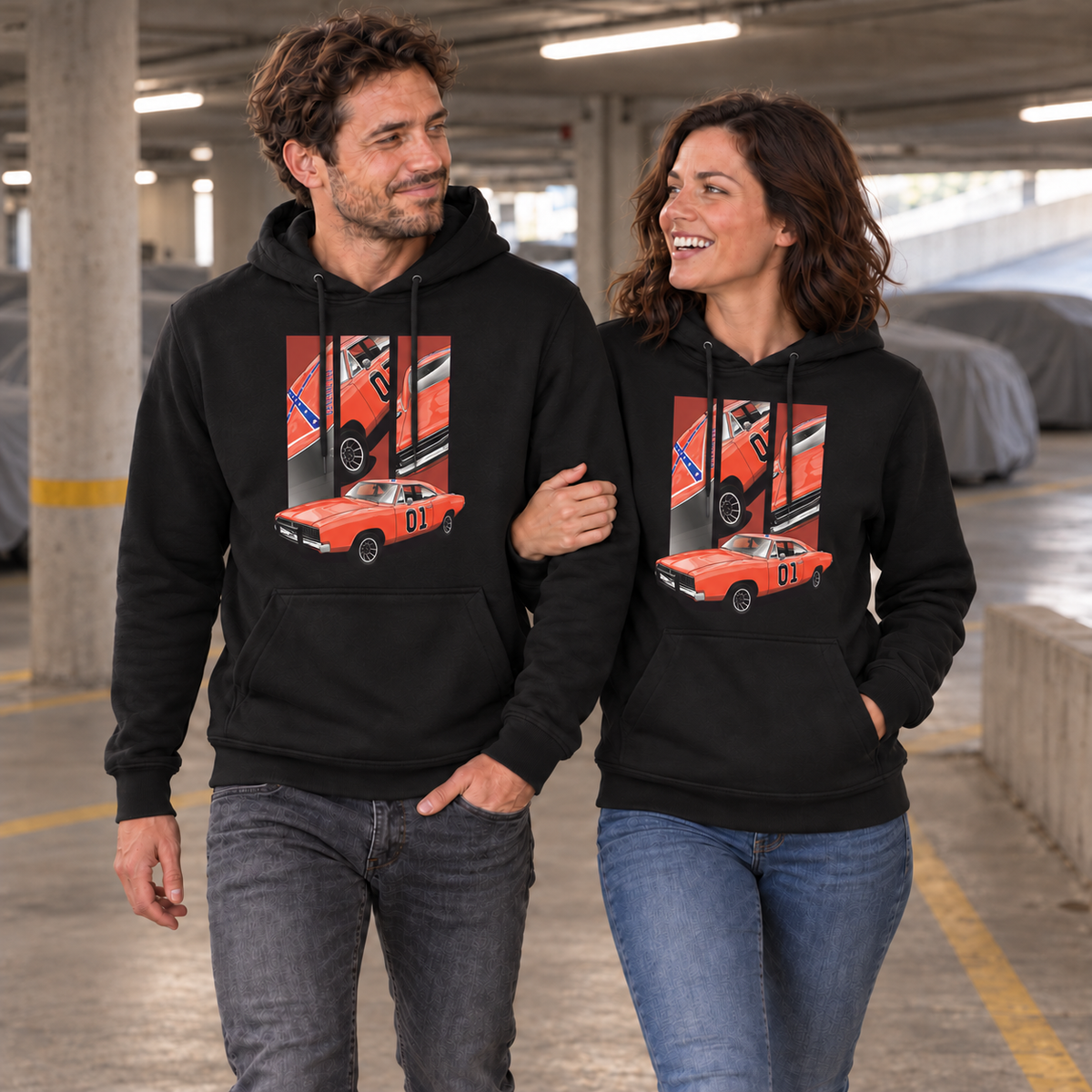 Paar in schwarzen Hoodies steht in einer Garage. Die Frau hält den Arm des Mannes; beide Vorderseiten zeigen das orange Fahrzeugmotiv mit der Zahl 01.