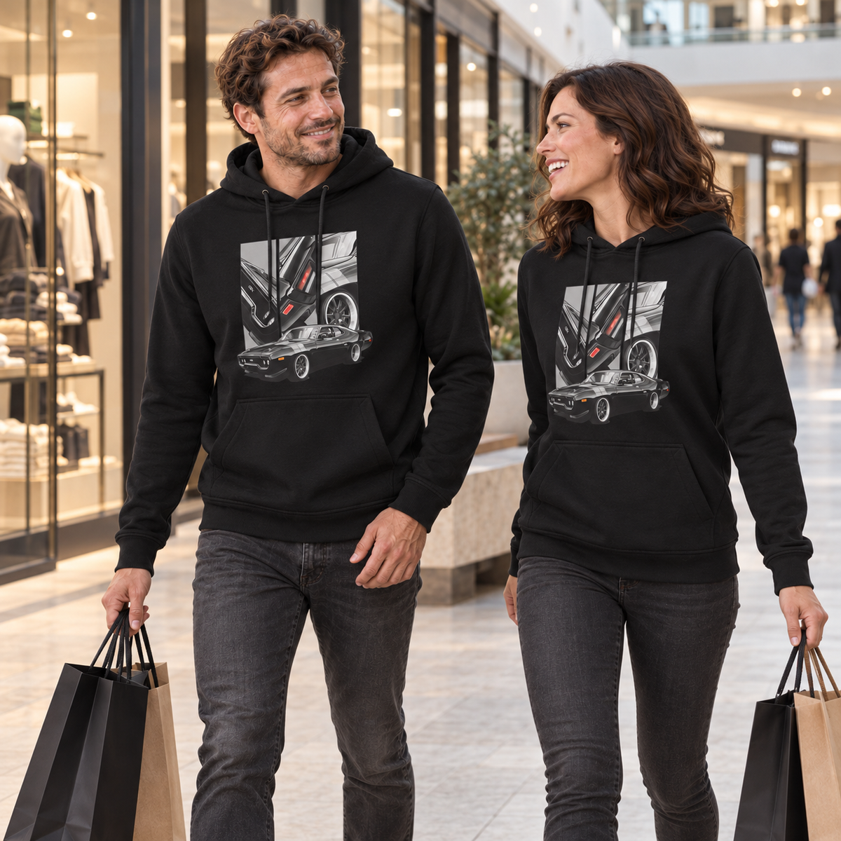 Paar in schwarzen Hoodies geht mit Einkaufstaschen durch eine Passage und sieht sich an. Beide Fronten zeigen das dunkle Coupé mit drei Detailfeldern.
