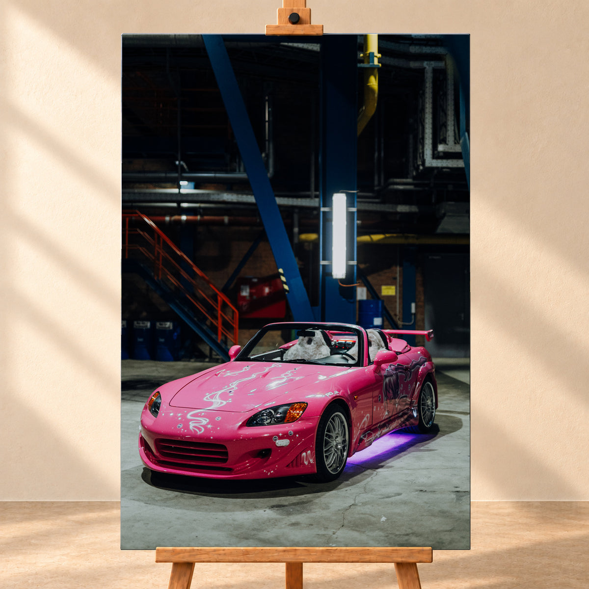 Frontale Visualisierung eines hochformatigen Leinwandbilds auf einer Holzstaffelei vor heller Wand. Das Motiv zeigt den pinken Honda S2000 aus „2 Fast 2 Furious“ mit weißem Dekor und violetter Unterbodenbeleuchtung in einer dunklen Industriehalle.