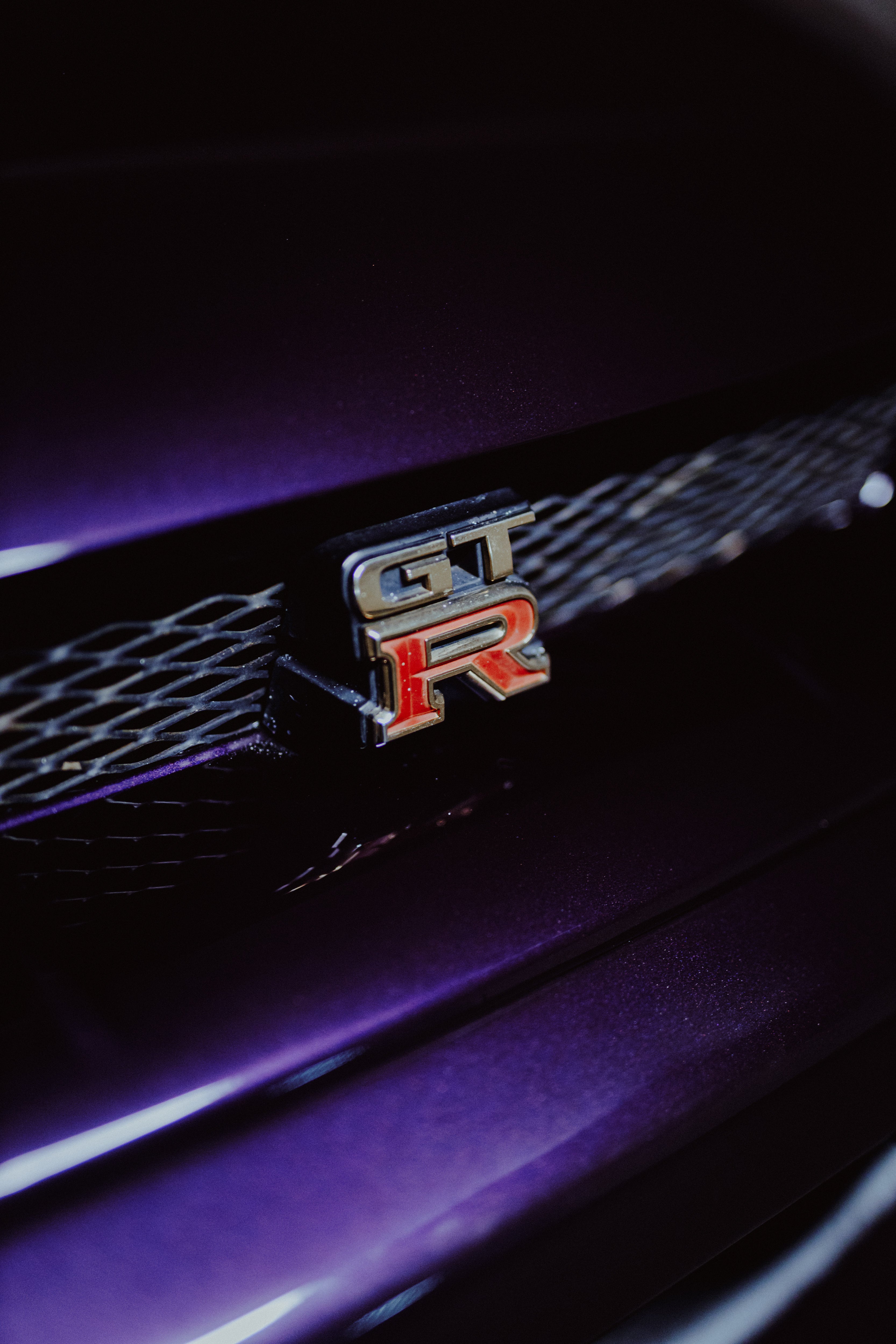 Schräg fotografiertes GT-R-Emblem im schwarzen Kühlergrill des violetten Nissan Skyline R33 GT-R NMP1.