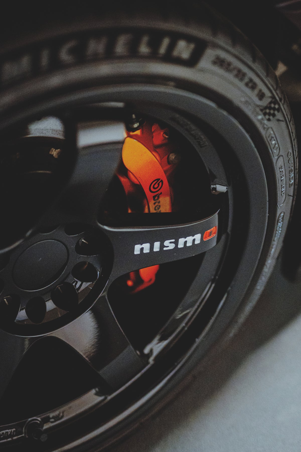 Schwarze Felge mit Nismo-Schriftzug und orangefarbenem Bremssattel hinter den Speichen.