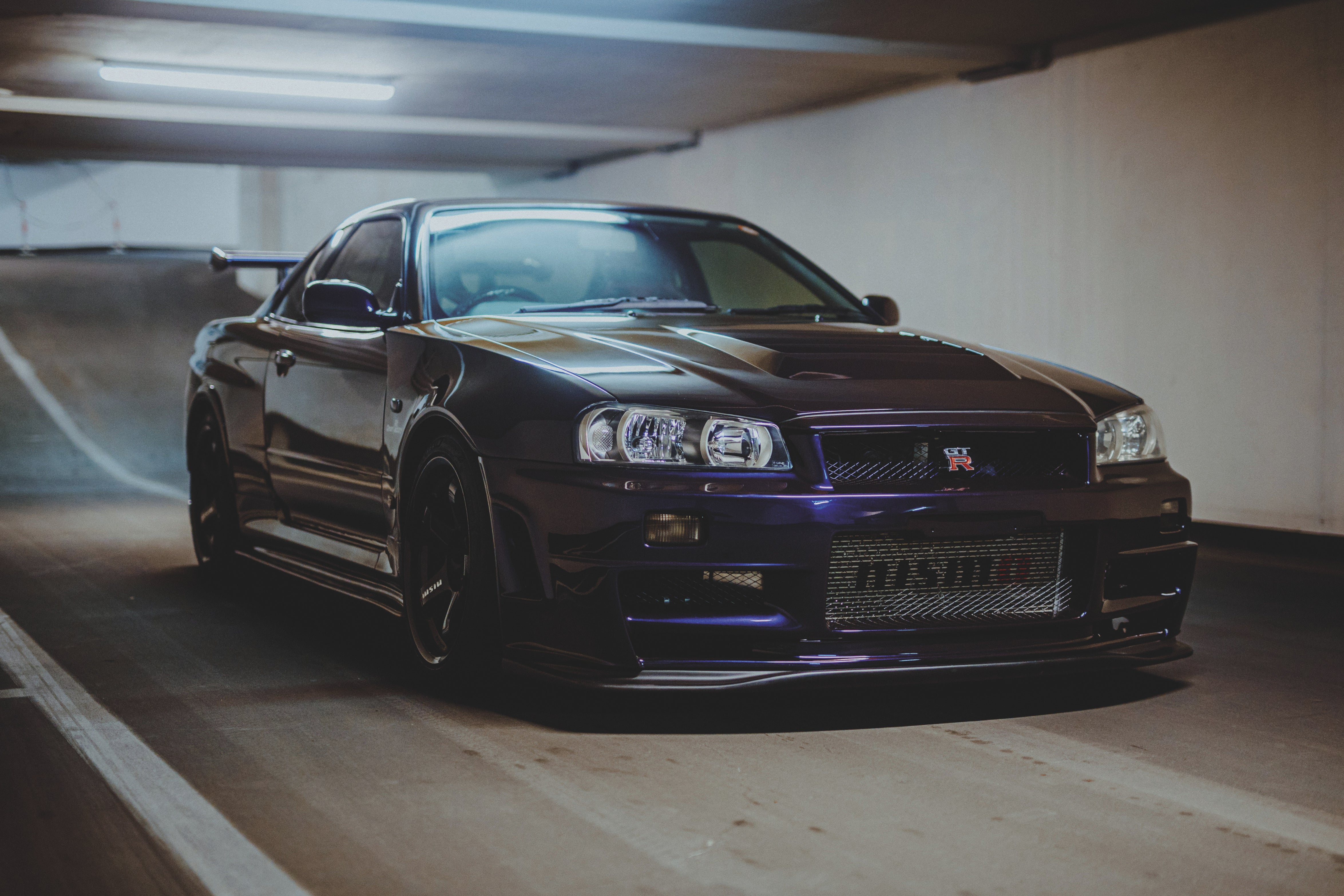 Nissan Skyline R34 schräg von vorn vor einer Garagenrampe, mit hellem Deckenlicht auf der Motorhaube.