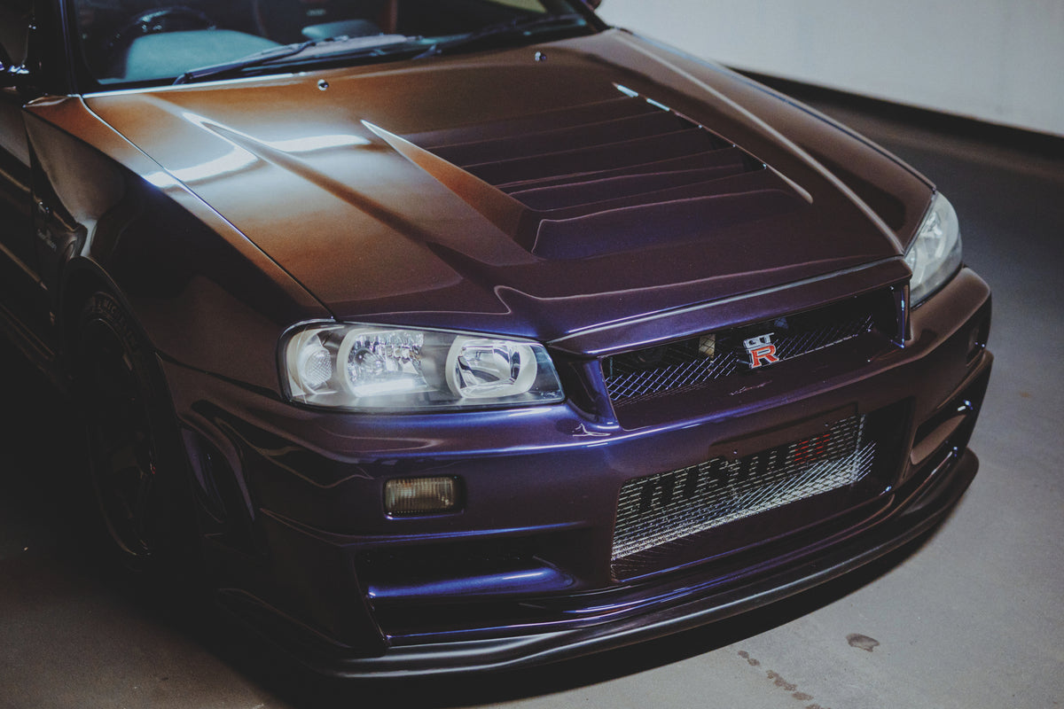 Schräger Blick von oben auf Motorhaube, Scheinwerfer und Frontgrill eines dunklen Nissan Skyline R34.