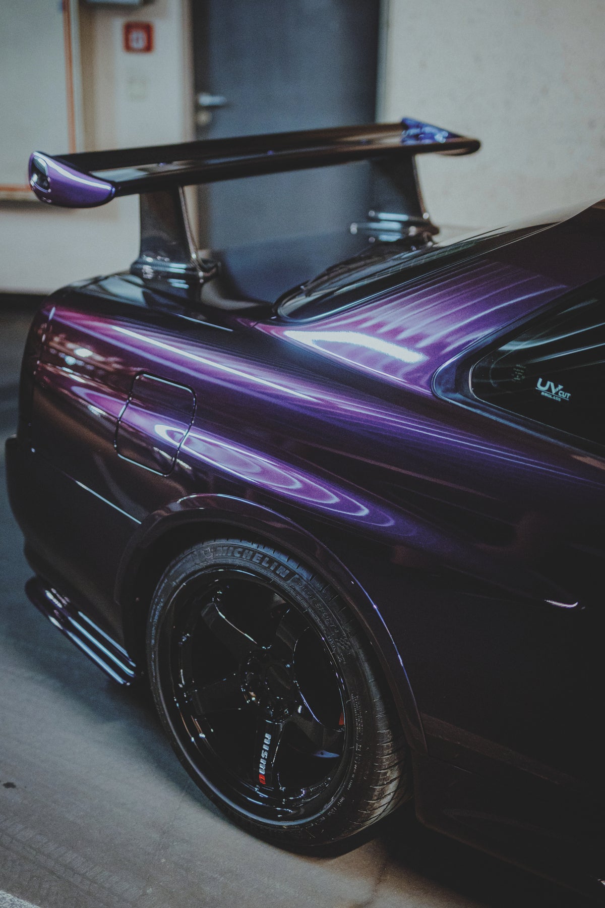 Nahansicht des violetten hinteren Seitenteils eines Nissan Skyline R34 mit schwarzem Rad und Heckflügel.